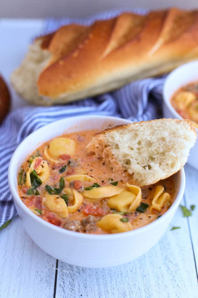 Sausage and tortellini soup in a white bowl with baguette 