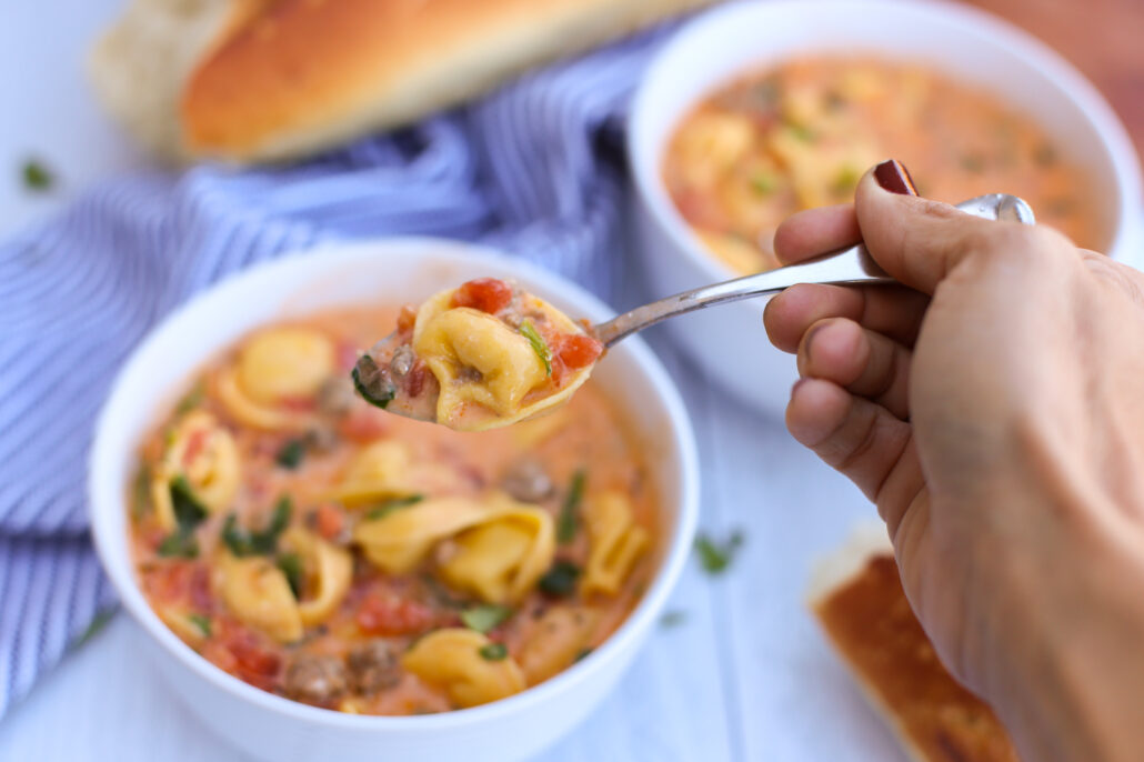 A spoon scooping some sausage tortellini soup from a bowl
