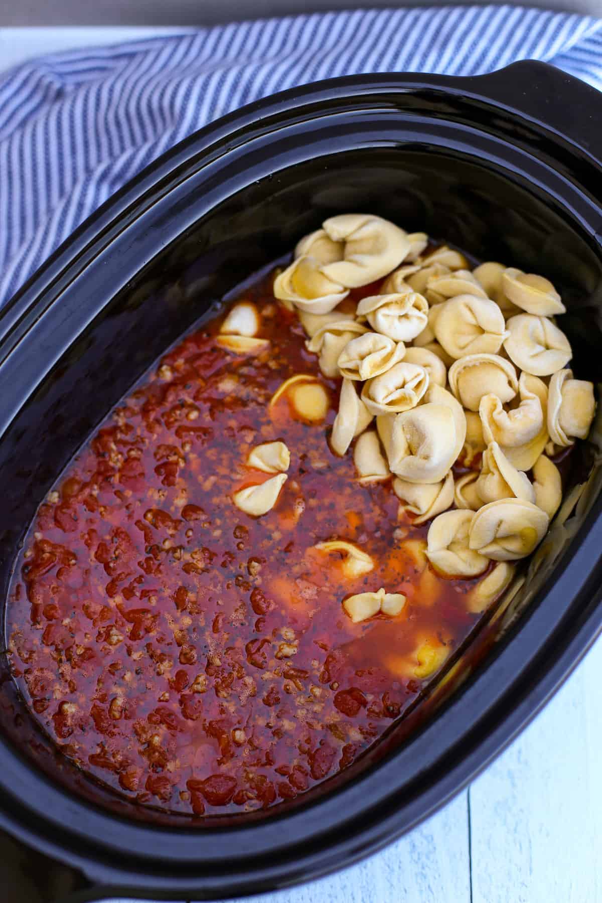 Adding frozen tortellini to the soup in a crock pot.