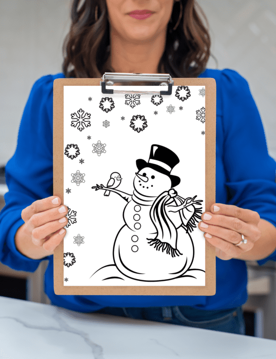 Hands holding a snowman coloring page on a clipboard.