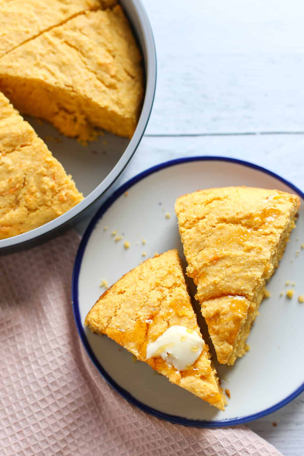 Sweet potato corn bread in a pan sliced in triangles with two pieces on a plate with butter on top.