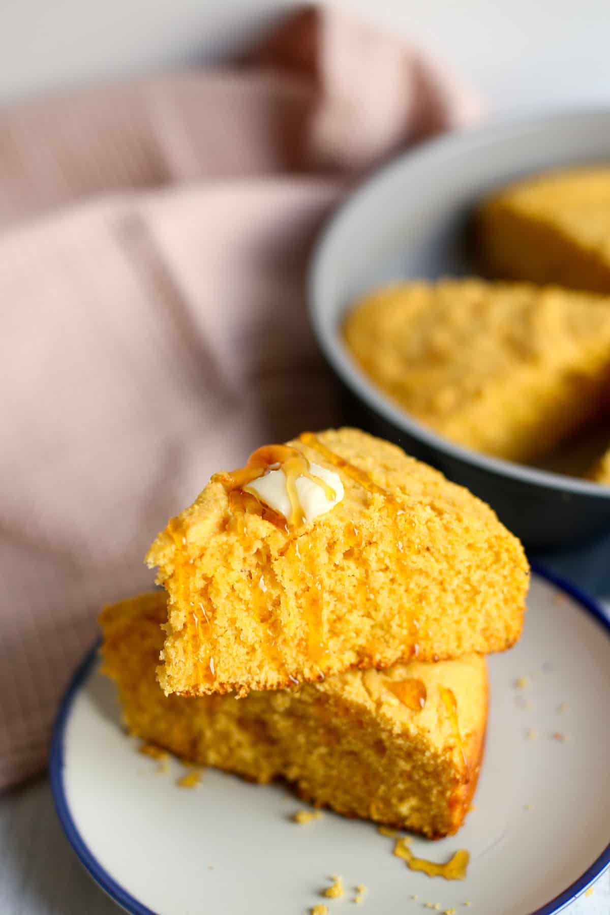 Two pieces of sweet potato corn bread stacked on a plate with a pat of butter and a drizzle of honey on top.