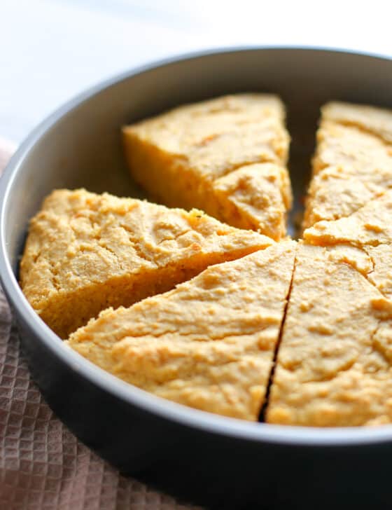 Baked sweet potato corn bread in a round metal dish with a slice missing.