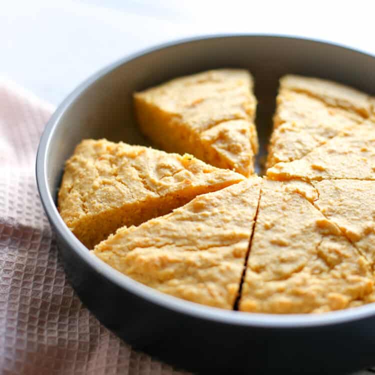 Baked sweet potato corn bread in a round metal dish with a slice missing.