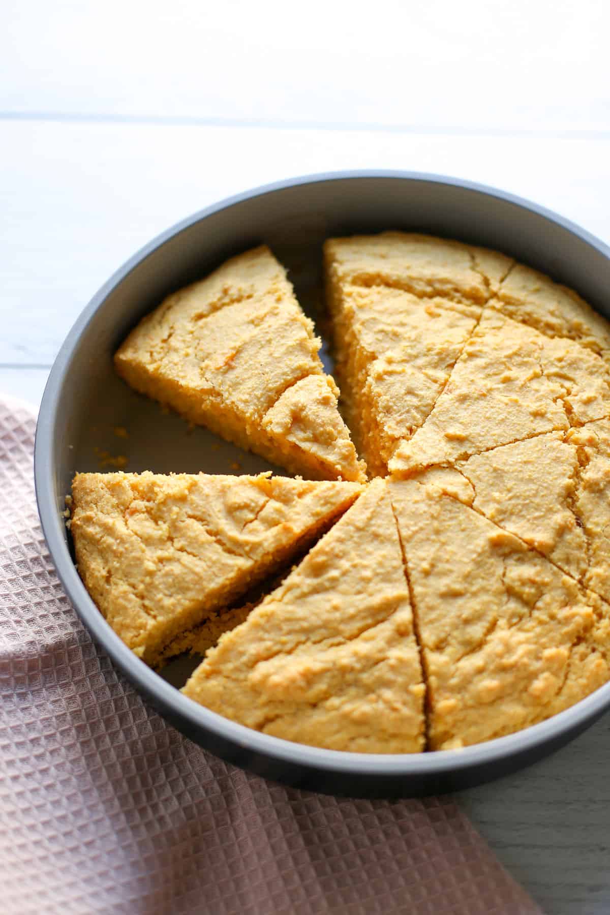 Baked sweet potato corn bread in a round metal pan with slices cut and one missing.