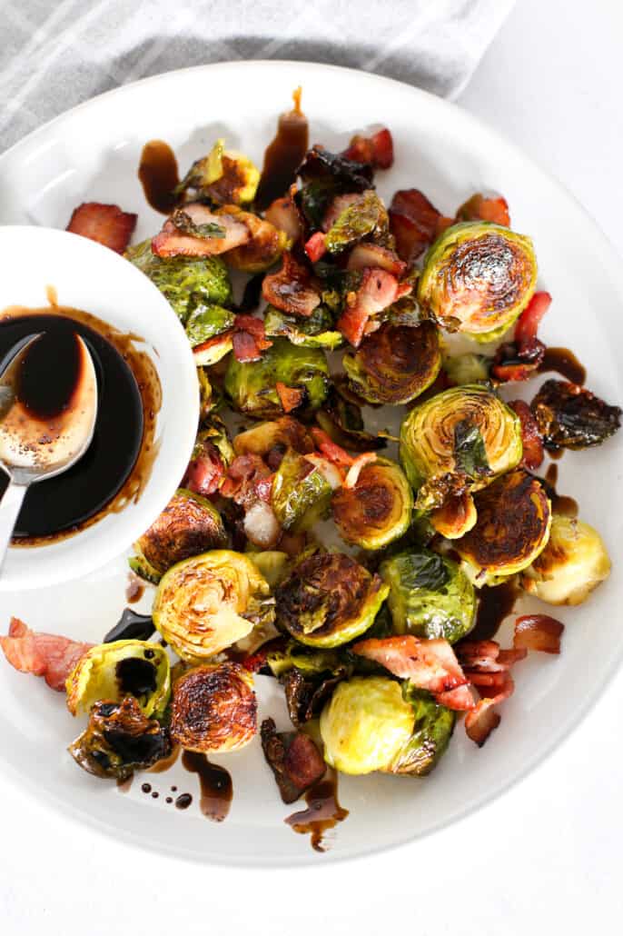 honey balsamic brussels sprouts on a white plate with bowl of balsamic reduction