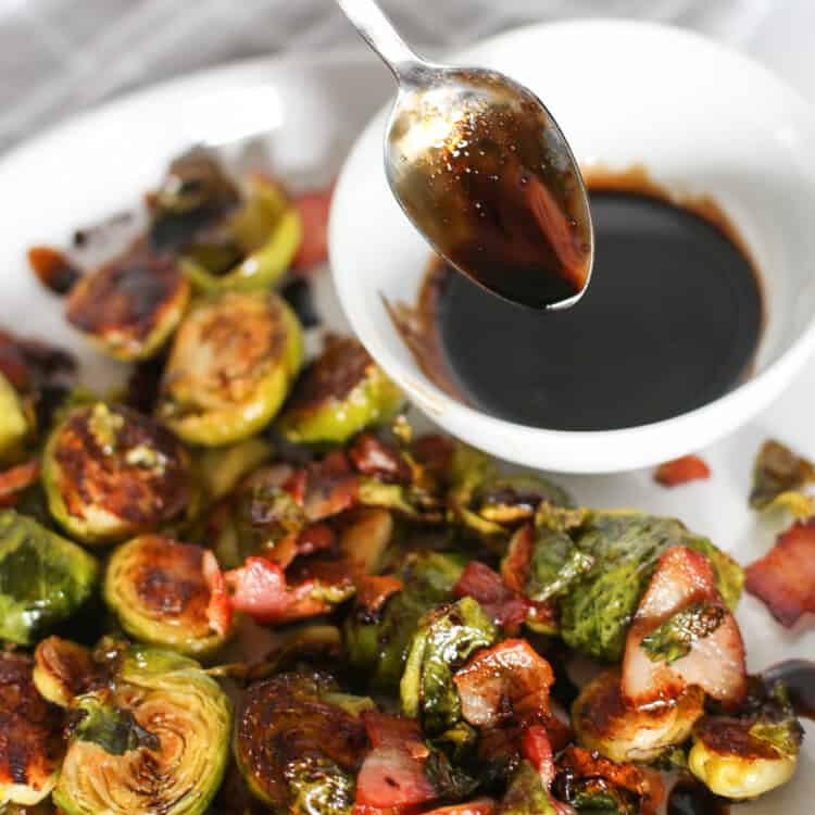 Honey balsamic Brussels sprouts on a white plate being drizzled with balsamic reduction.