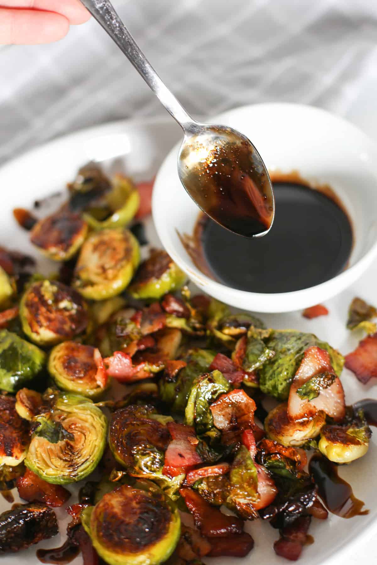 Honey balsamic Brussels sprouts on a white plate being drizzled with a balsamic reduction.