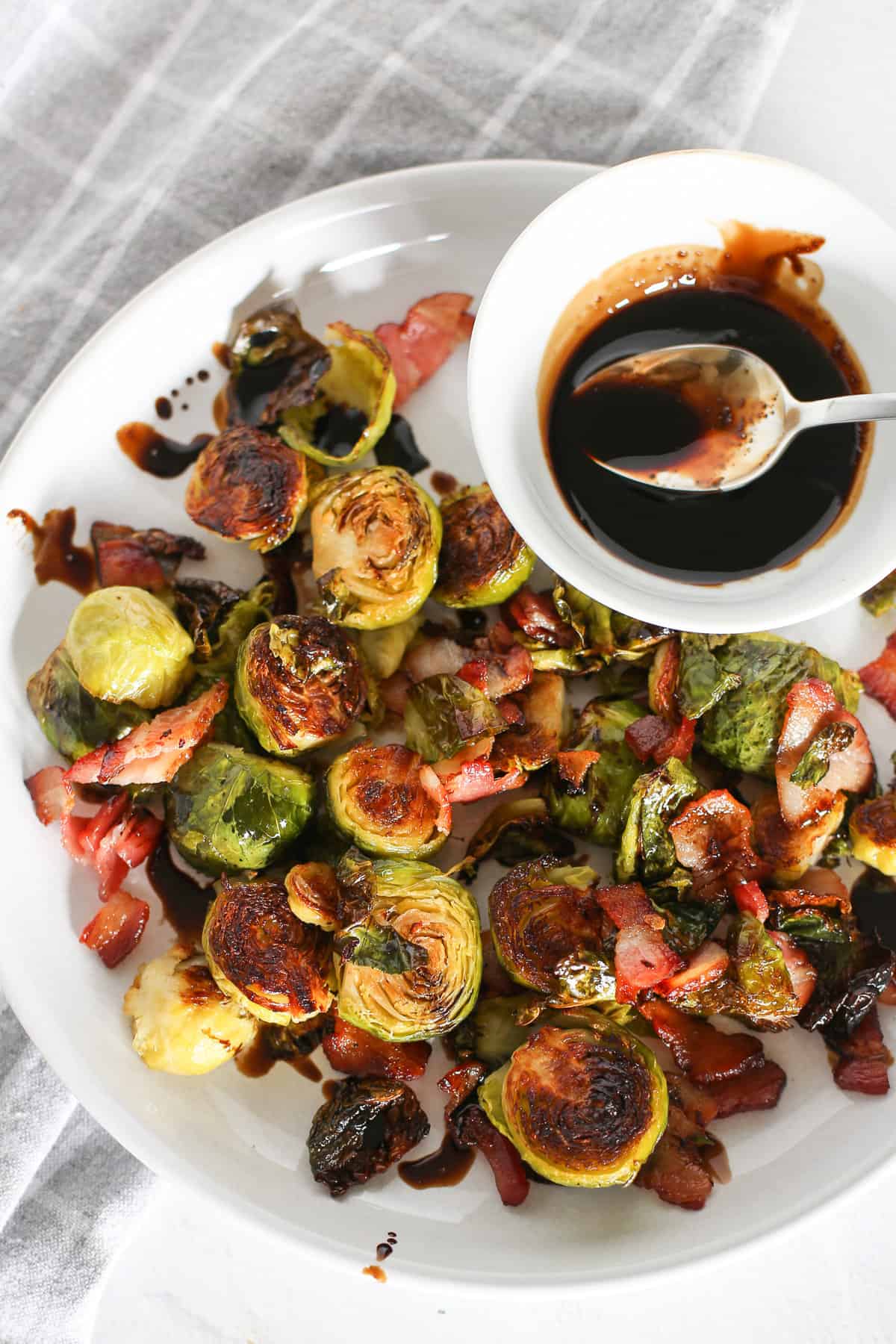 Oven-roasted Brussels sprouts on a white plate being drizzled with a honey balsamic reduction.