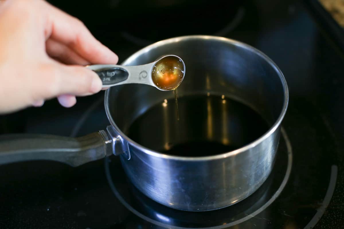 Someone pouring honey from a measuring spoon into a sauce pan with balsamic vinegar.