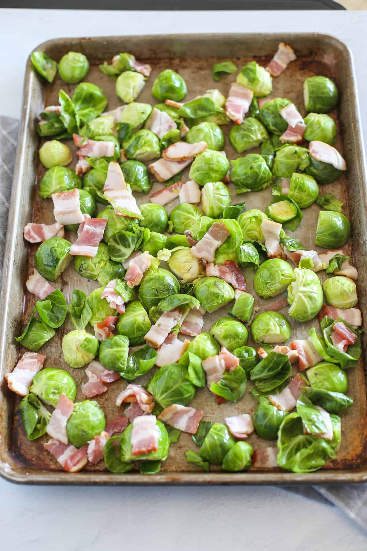 Uncooked chopped brussels sprouts and chopped bacon on a baking sheet ready for the oven.