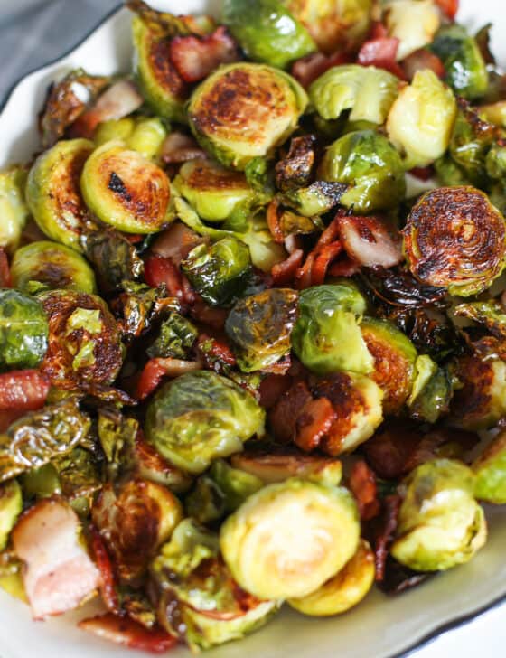 A hand holding a serving dish of roasted Brussels Sprouts with Bacon.
