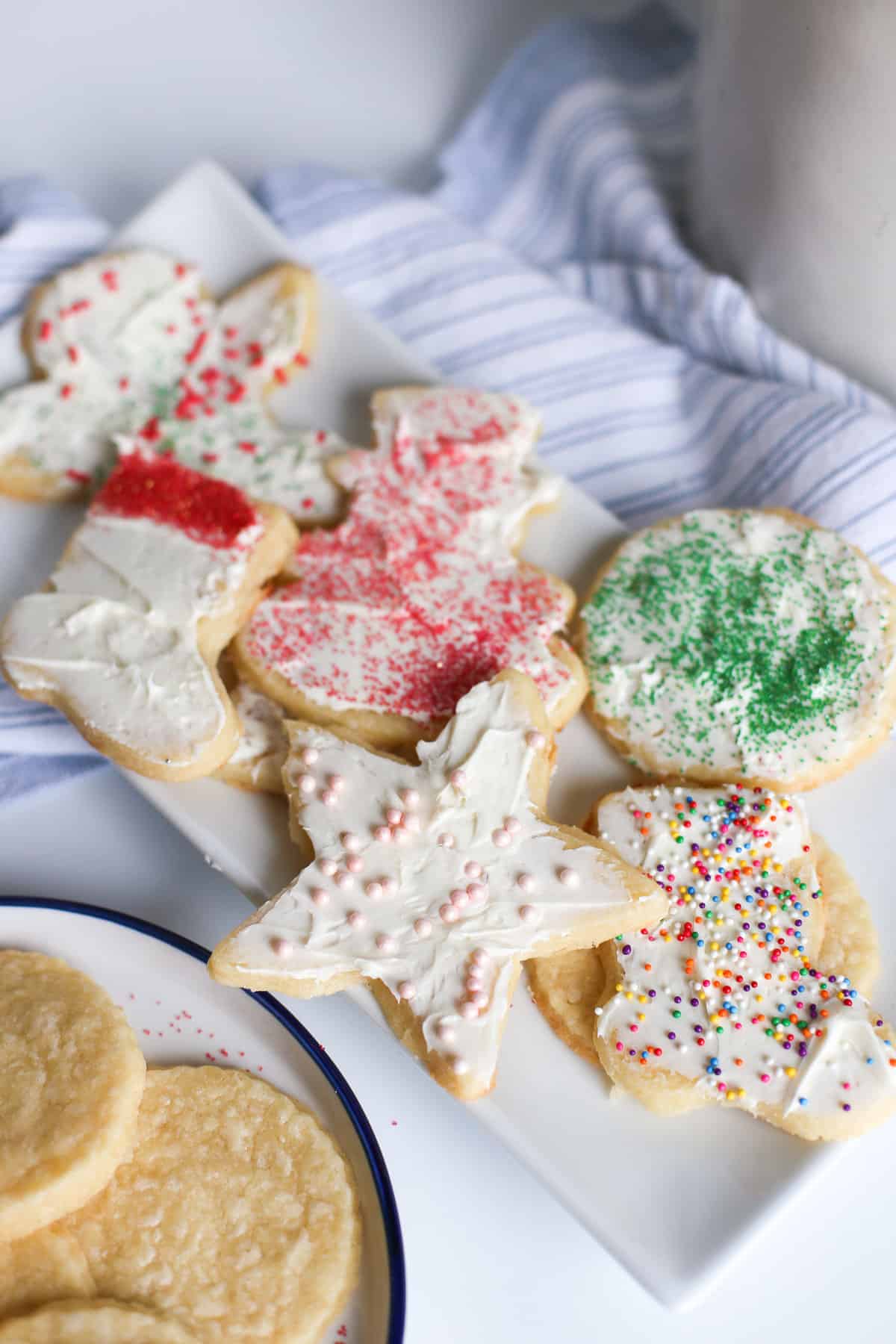 Decorated cream cheese sugar cookies on a platter with some undecorated ones on a plate next to it.