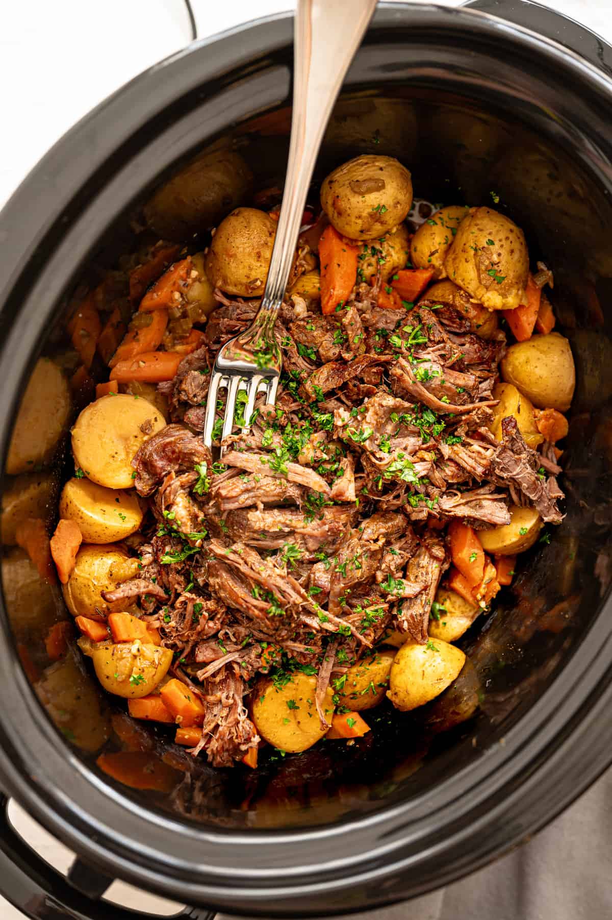 Yukon gold potatoes and carrots around the edge of a slow cooker with shredded pot roast in the middle ready to serve.