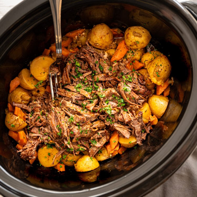 Cooked roast in a crockpot with potatoes and carrots around the edges waiting to be served.