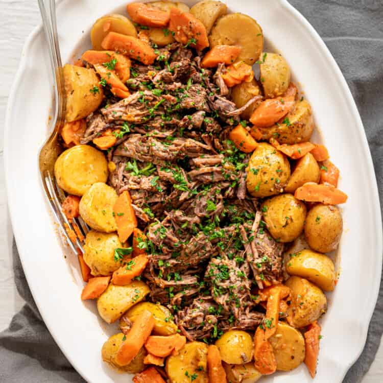 Shredded pot roast on a platter surrounded by potatoes and carrots.
