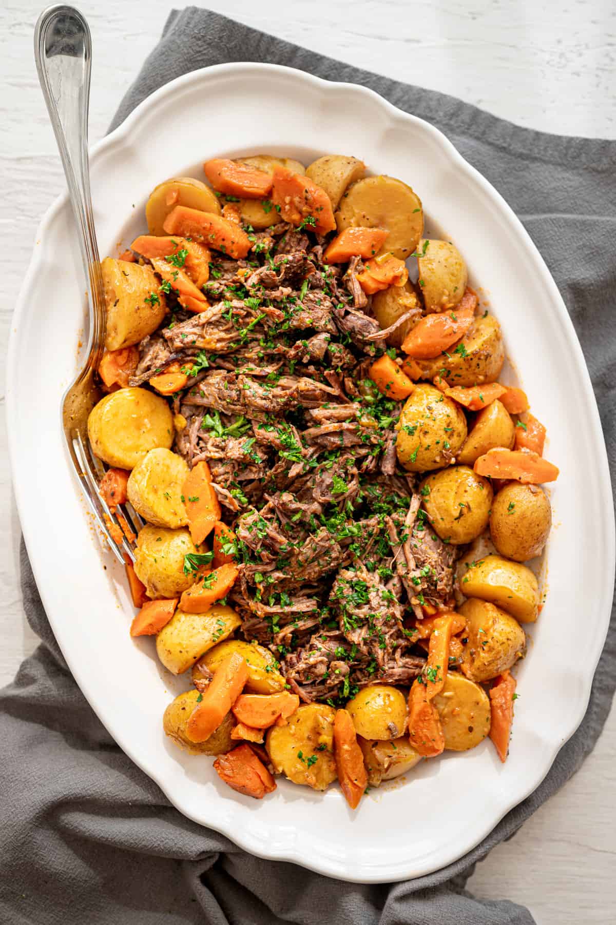 Pot roast on a platter in the middle of Yukon gold potatoes and carrots.