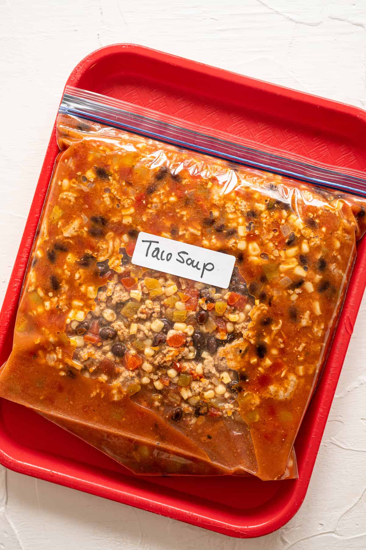 A full gallon-size freezer bag labeled taco soup lying flat on a tray.