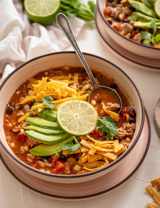 Bowl of taco soup with sliced avocado and tortilla strips on top.