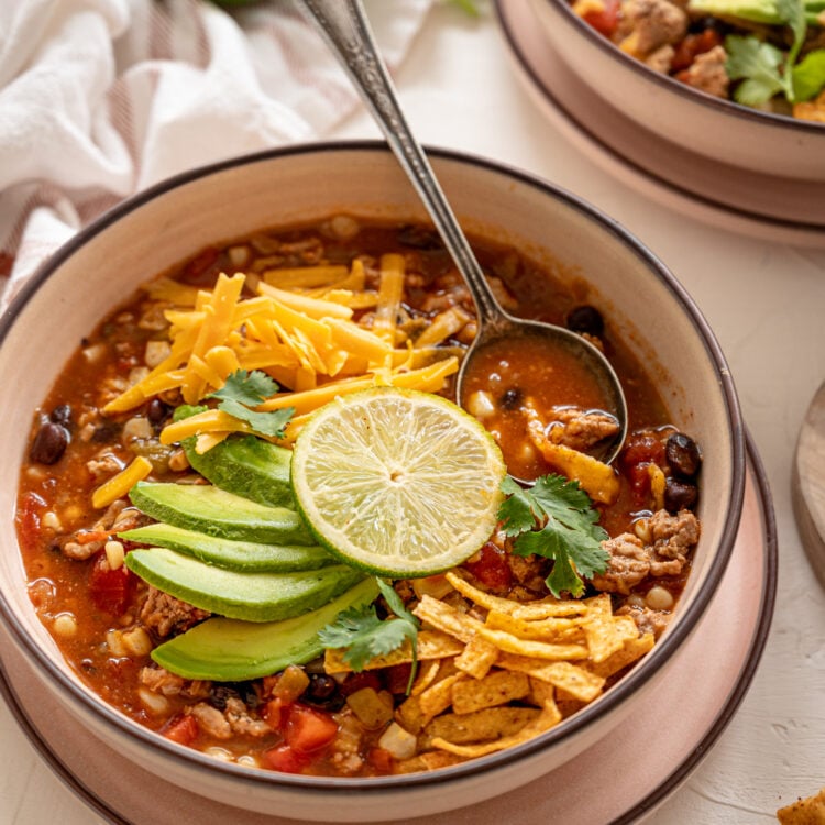 Bowl of taco soup with sliced avocado and tortilla strips on top.