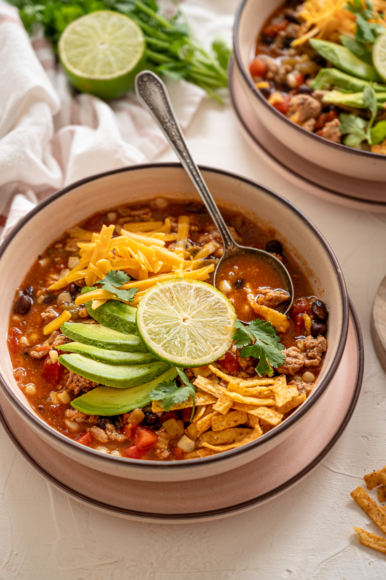 Taco soup made with ground beef with sliced avocado and shredded cheddar cheese on top.