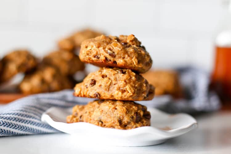 Three breakfast cookies stacked on a plate with more cookies in the background.