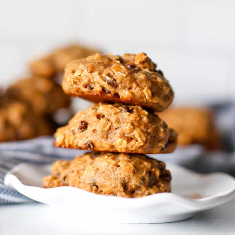 Three breakfast cookies stacked on a plate with more cookies in the background.