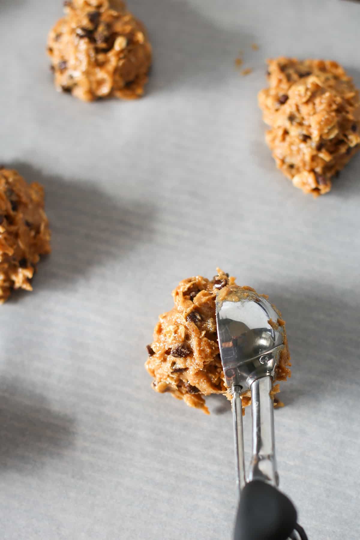 Breakfast cookie dough being scooped onto parchment paper on a cookie sheet.
