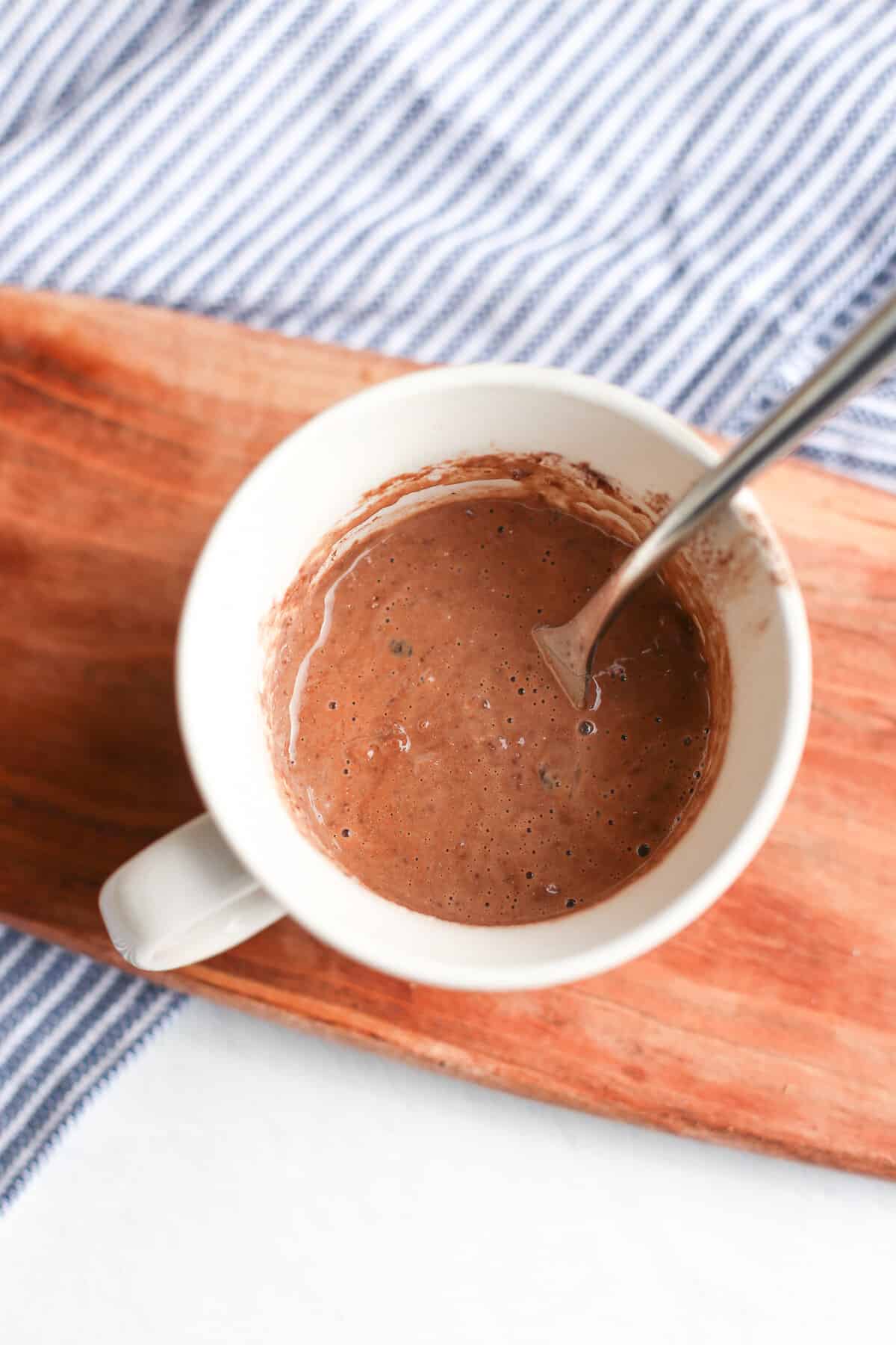 Cake batter in a coffee mug with a spoon, not yet cooked.