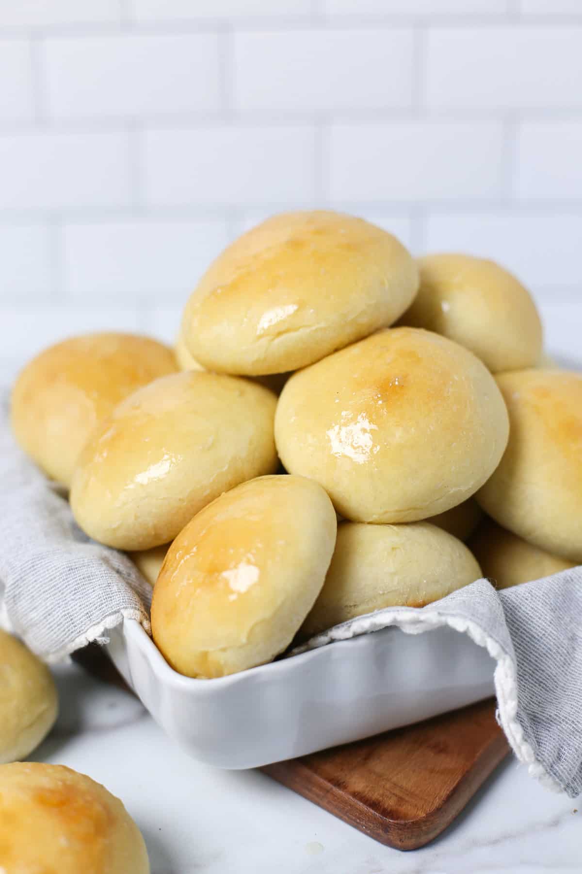 Bread machine dinner rolls stacked up in a serving dish that has a cloth napkin laid in it.