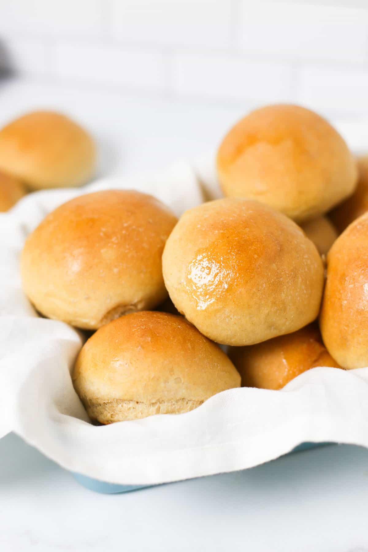 Bread machine wheat rolls stacked in a basket with a linen napkin lining it.