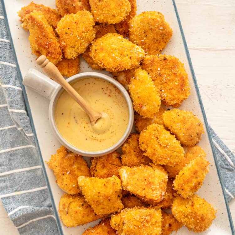 homemade chicken nuggets on a white platter with honey mustard dipping sauce in a bowl