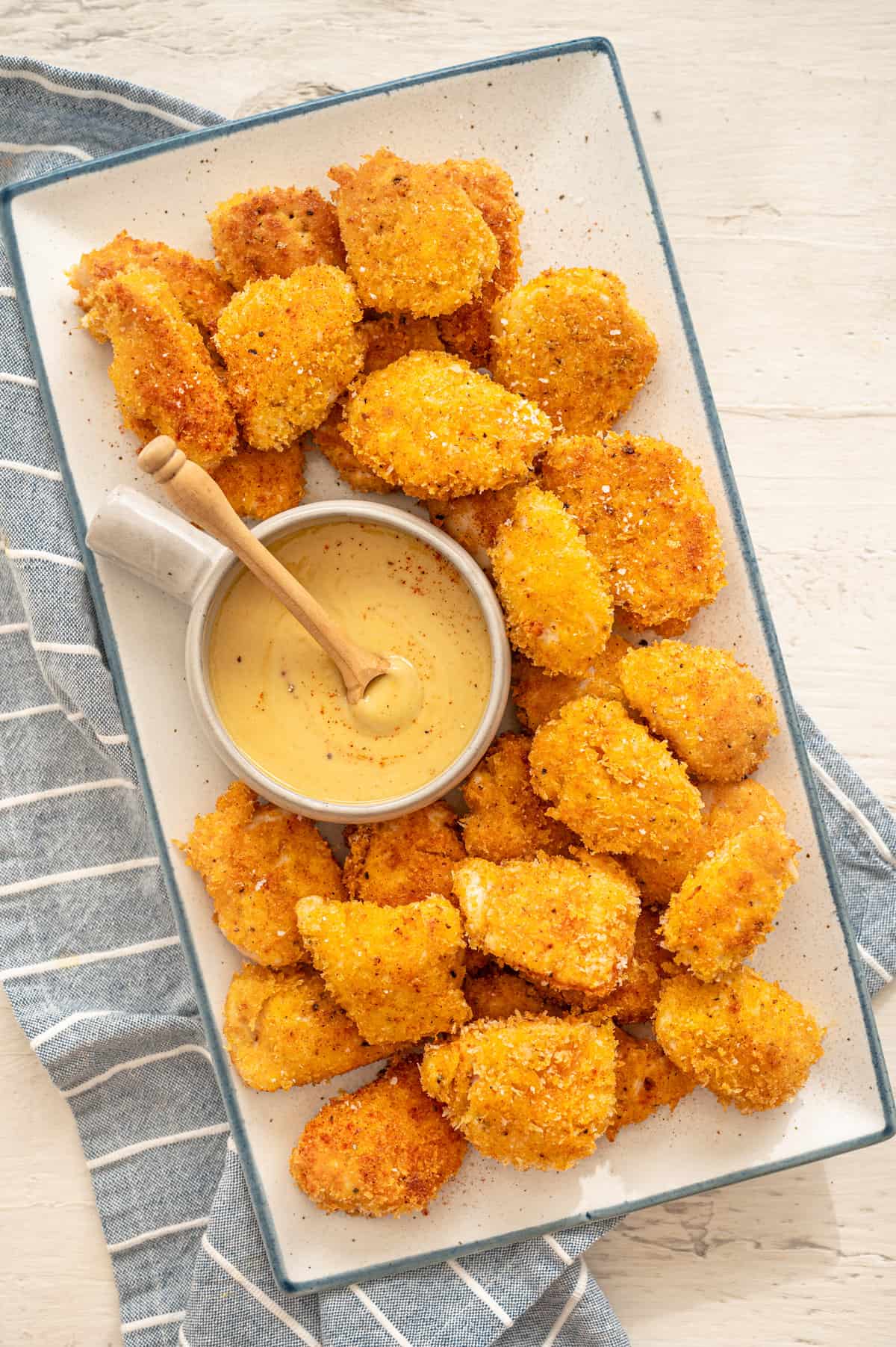 Homemade chicken nuggets on a white platter with honey mustard dipping sauce in a bowl.