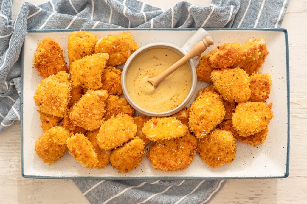 homemade chicken nuggets on a white platter with honey mustard dipping sauce in a bowl