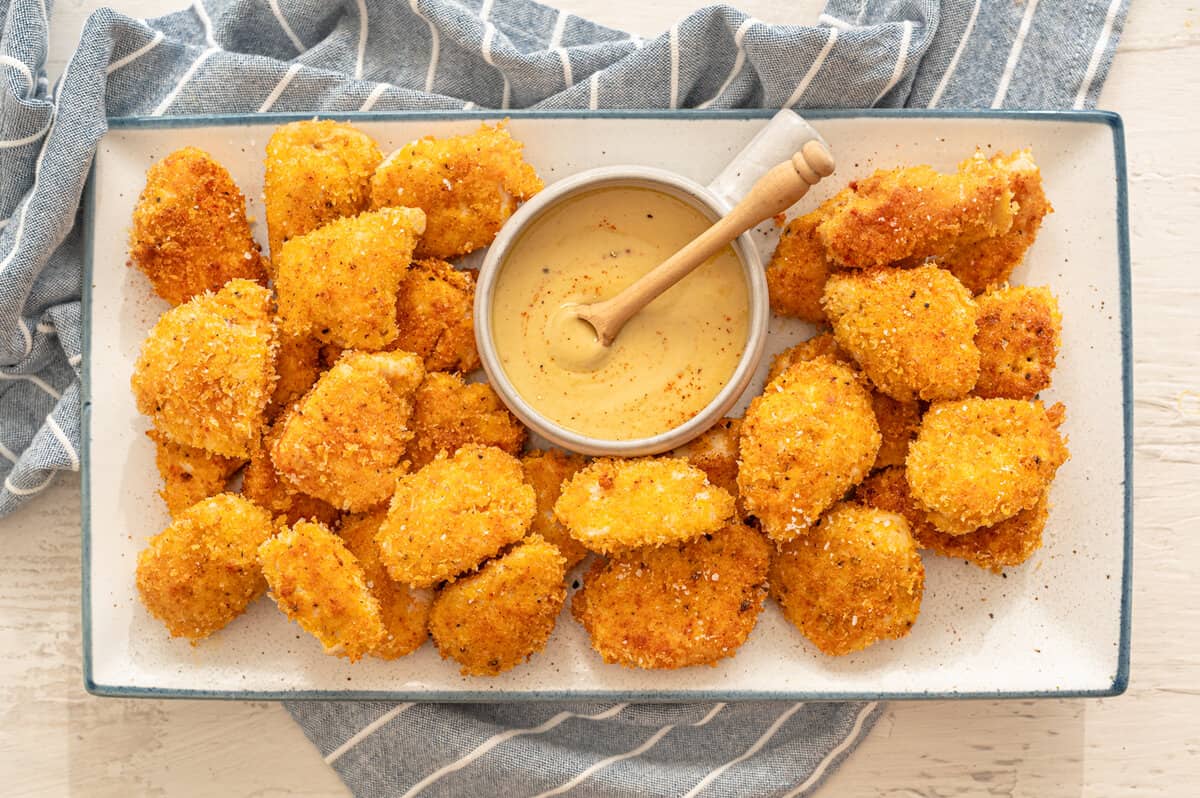 Homemade chicken nuggets on a white platter with honey mustard dipping sauce.