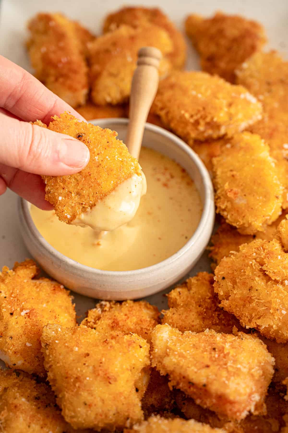 Hand dipping a chicken nugget into honey mustard dripping sauce.
