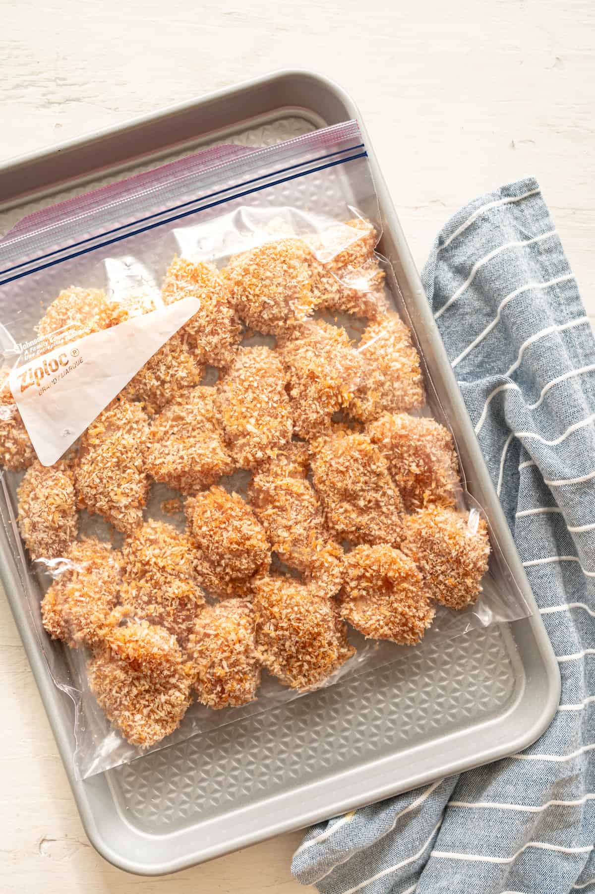 Uncooked homemade chicken nuggets in a freezer bag on a baking sheet.