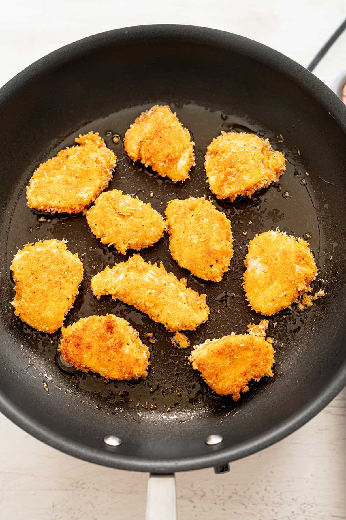 Chicken nuggets cooking in a skillet with a little oil.