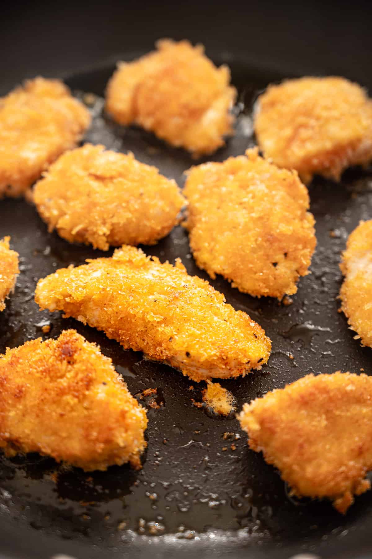 Chicken nuggets cooking in a pan to show crispy exterior.