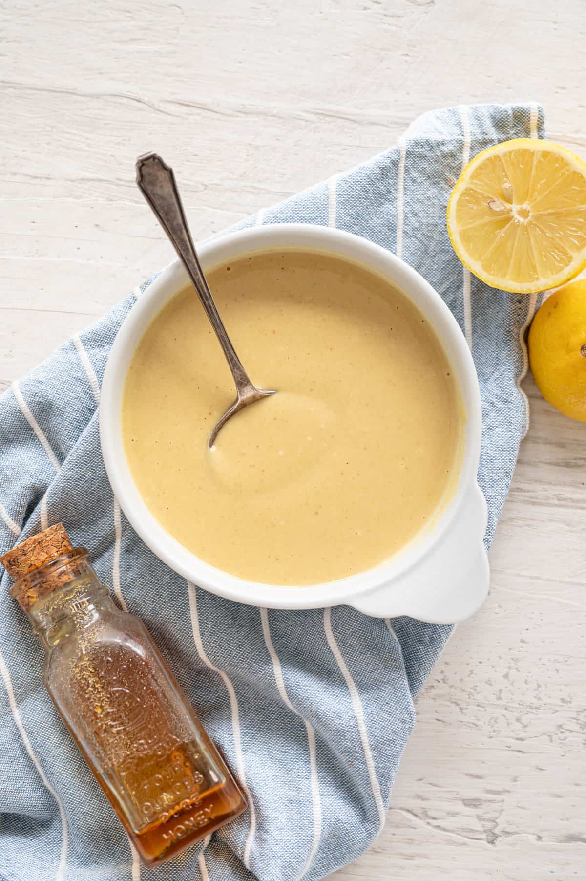 Honey mustard dipping sauce in bowl with spoon and lemons on the side.