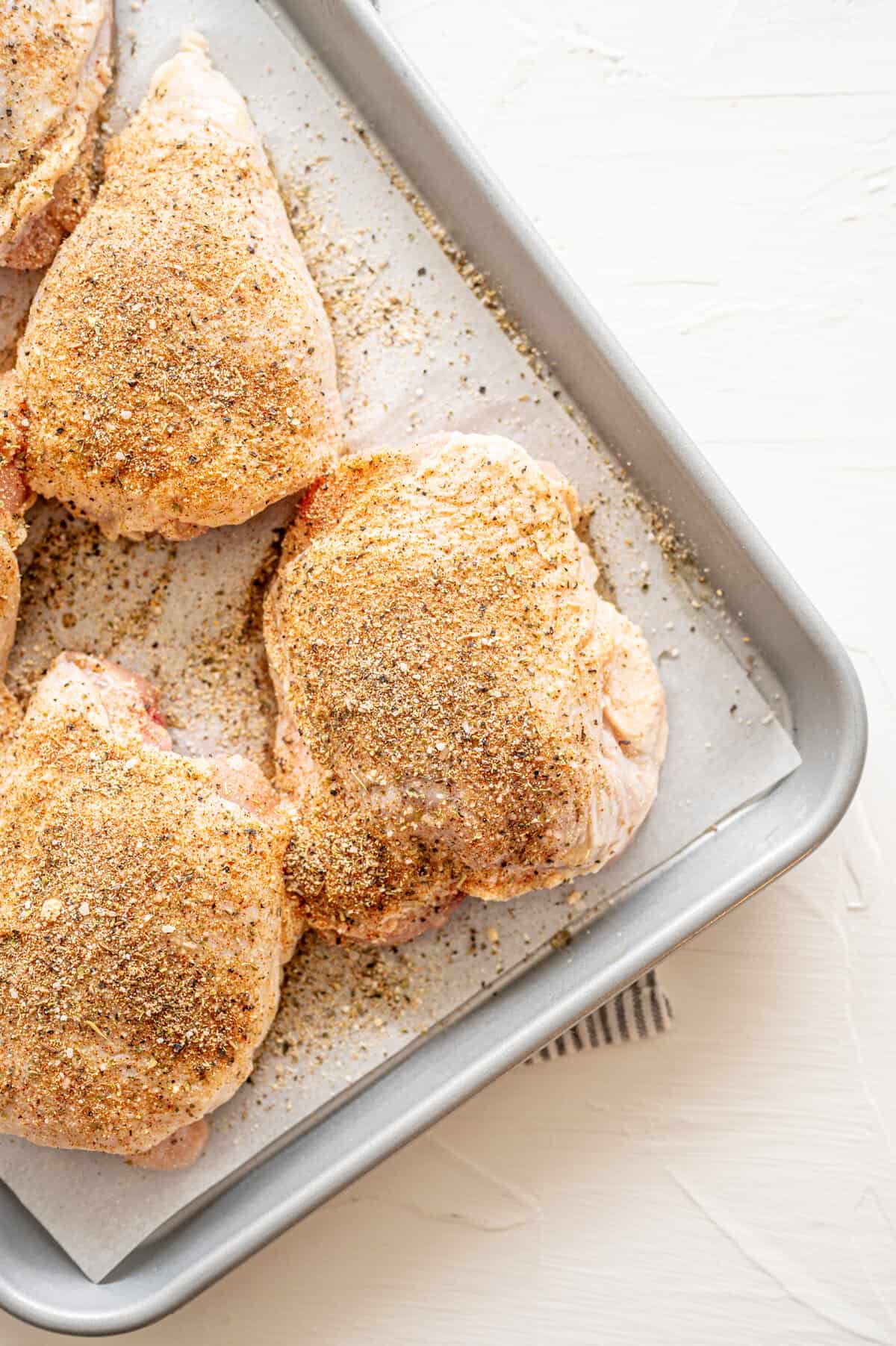 Seasoned chicken thighs on a baking sheet lined with parchment paper ready for the oven.