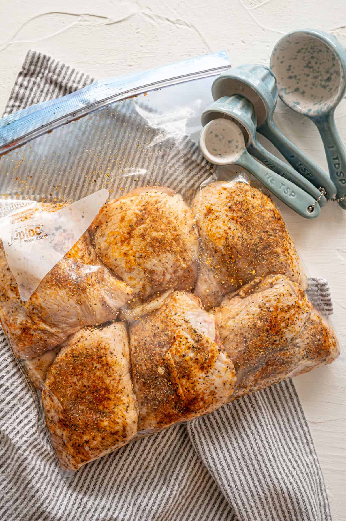 Italian chicken thighs packaged as a freezer meal with uncooked chicken thighs covered in seasoning in a freezer bag.