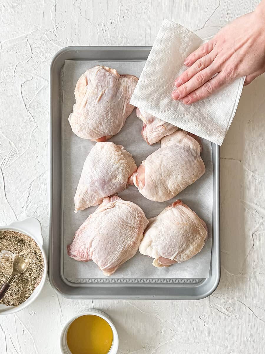 Someone patting chicken thighs dry with a paper towel.