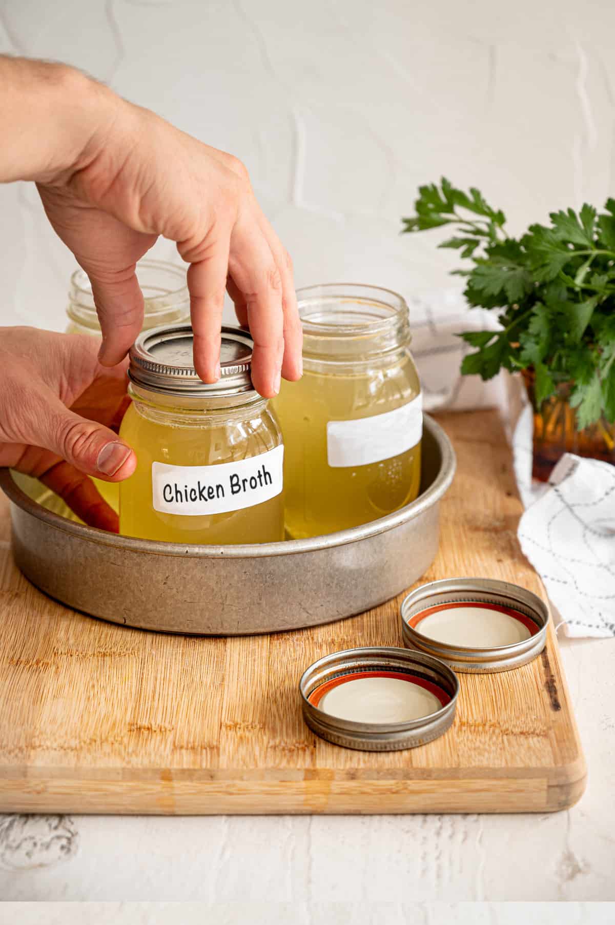 A hand putting a lid on a full mason jar labeled chicken broth.