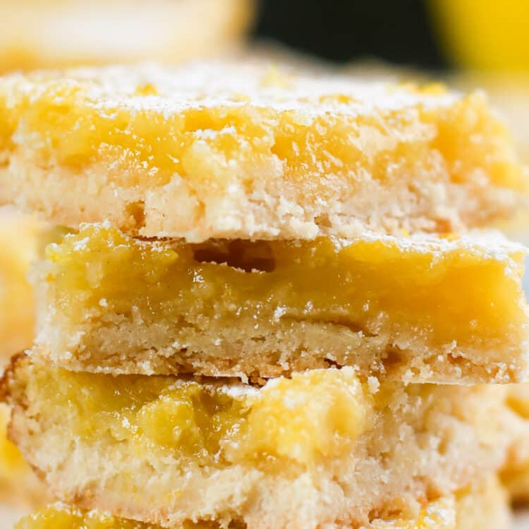 Lemon bars stacked up with powdered sugar sprinkled all over.