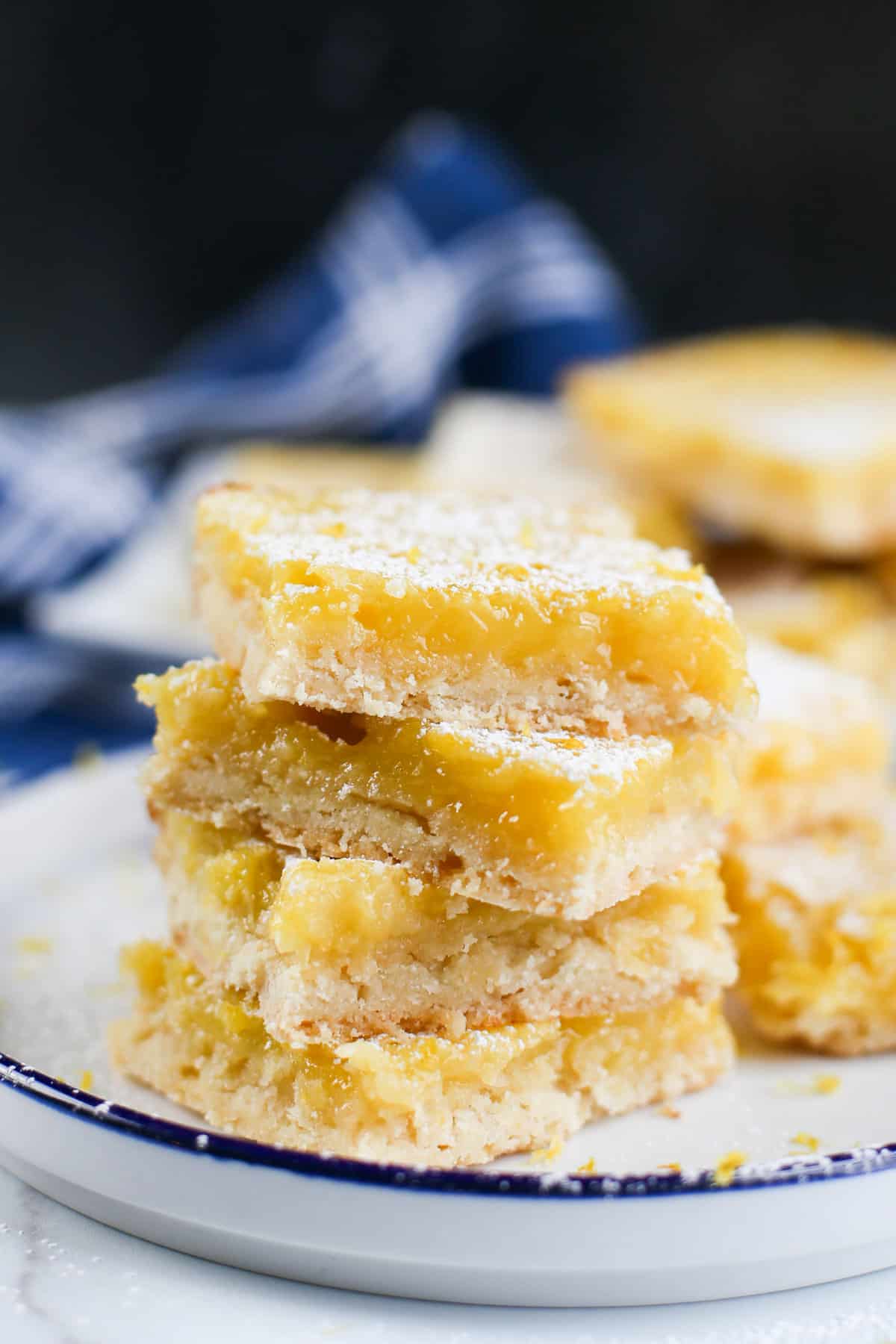 Lemon bars stacked up on a plate with powdered sugar sprinkled all over.