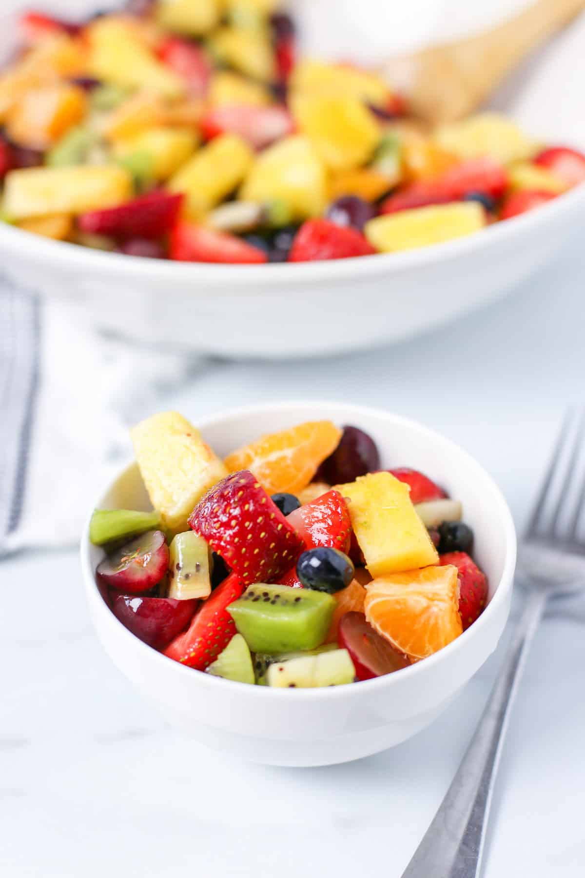 Fruit salad serving in a small white bowl with a fork next to it.