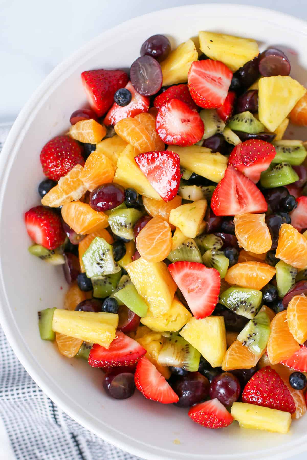 Fruit salad consisting of strawberries, clementines. grapes, kiwi, pineapple, and blueberries.