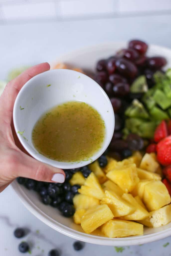 pouring fruit salad dressing over fruit salad