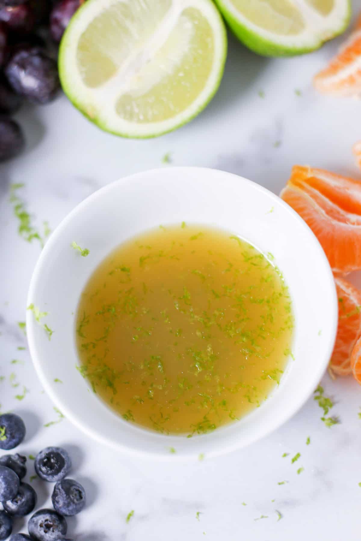 Fruit salad dressing in a white bowl with lime juice, honey, and lime zest.
